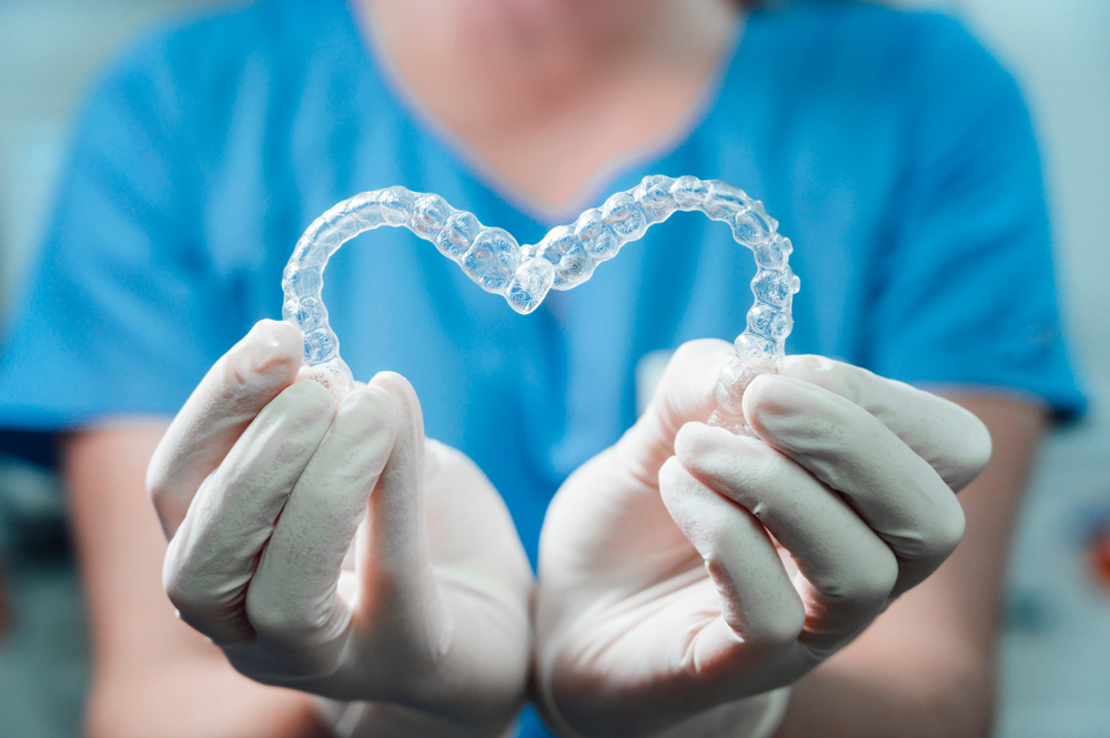 female,doctor,holding,two,transparent,heart shaped,dental,aligners